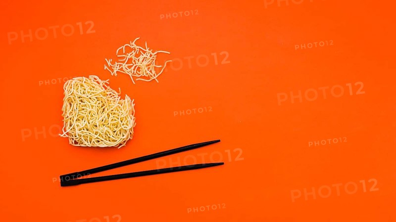Broken dry instant noodles with chopsticks orange background