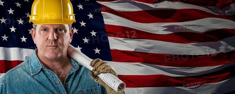 Male contractor wearing blank yellow hardhat over waving american flag background banner