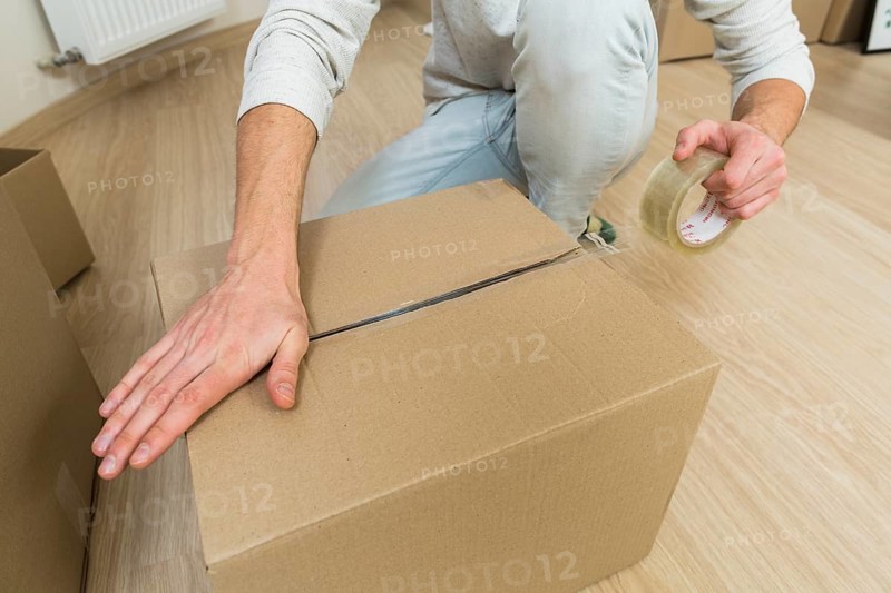 Close up male sealing cardboard box with adhesive tape