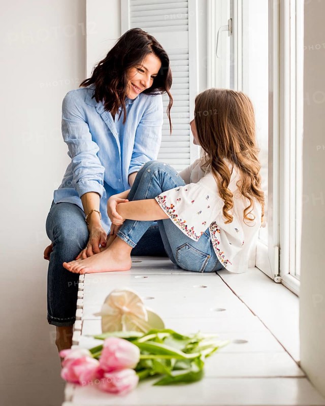 Happy mother daughter sitting window sill