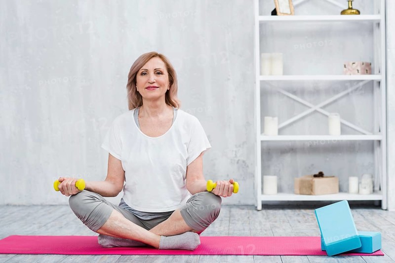 Portrait beautiful woman sitting yoga mat near blocks holding yellow dumbbells home