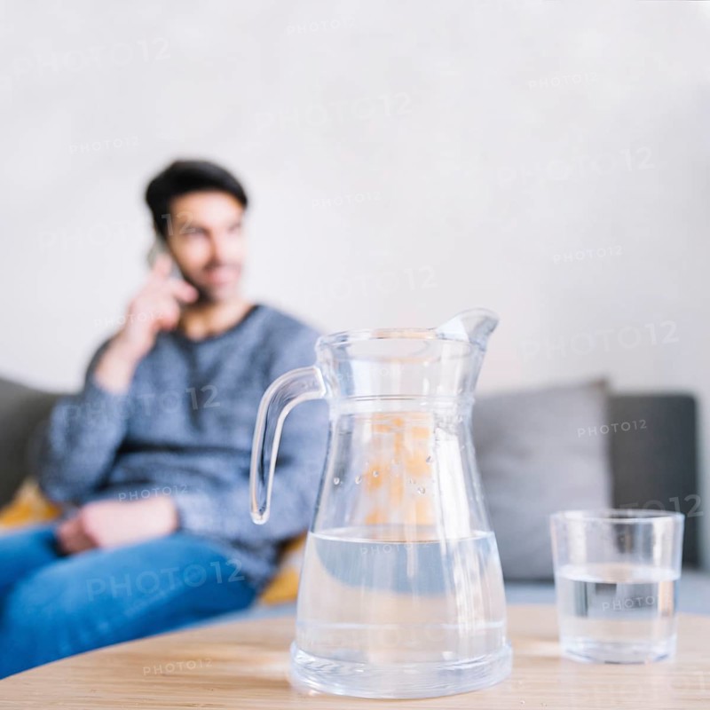 Glass jug near man with smartphone