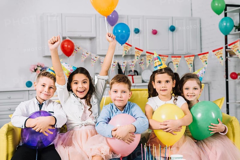 Portrait children sitting sofa holding balloons