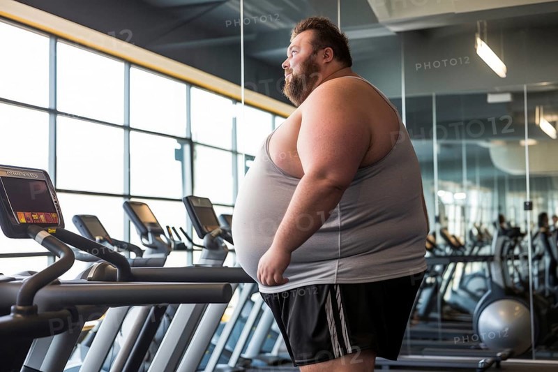 Very obese man stands in front of treadmills in gym