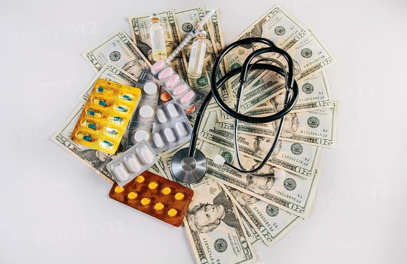 Top view of stethoscope with pills on money isolated. High cost of medical health with stethoscope and medicines. View of medical stethoscope with medicaments and money