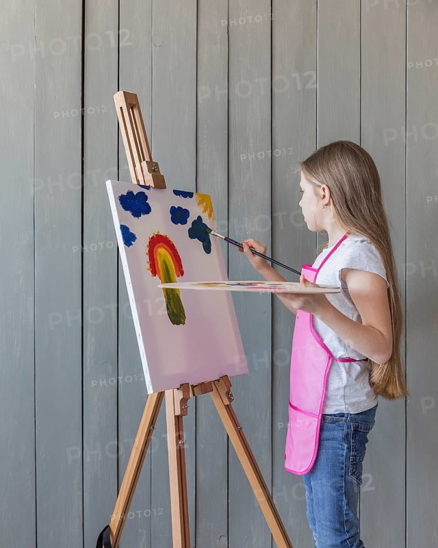 Side view girl drawing with paint brush easel against wooden plank