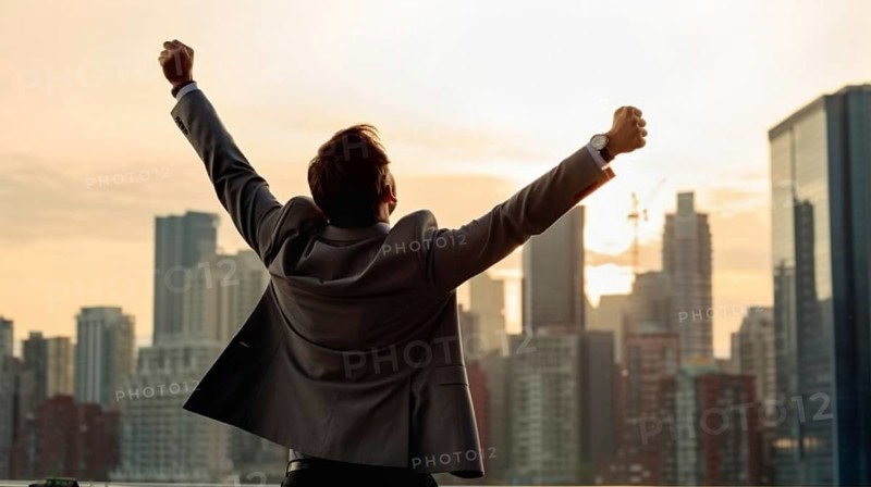 Excited businessman celebrates with his fists in the air with the city in the background