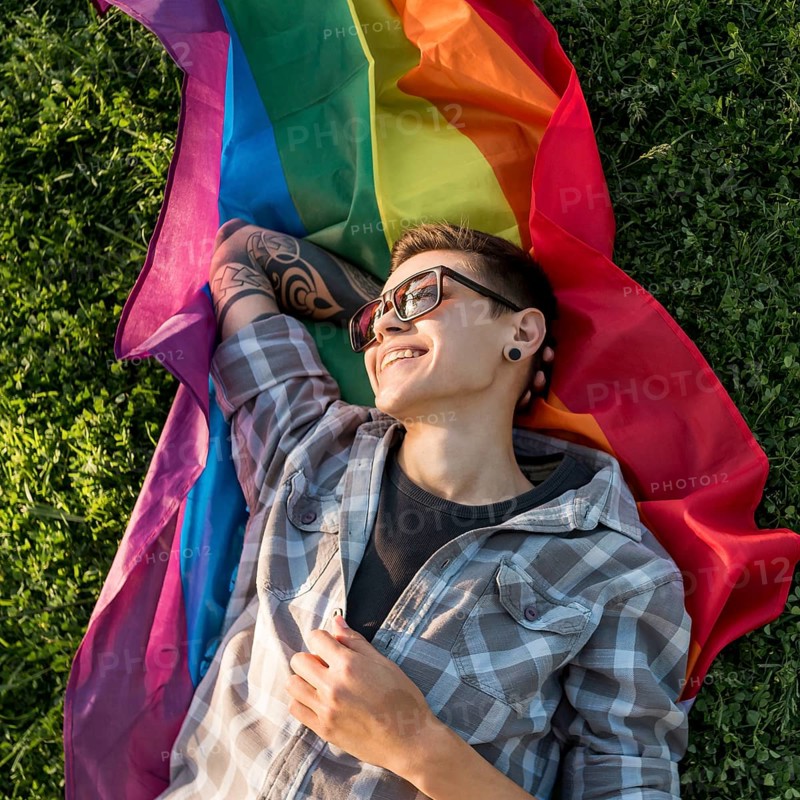 Cheerful young person lying lgbt flag park
