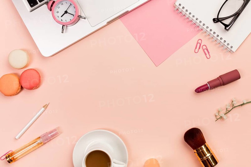 Macaroons coffee cup makeup brushes alarm clock laptop peach colored background