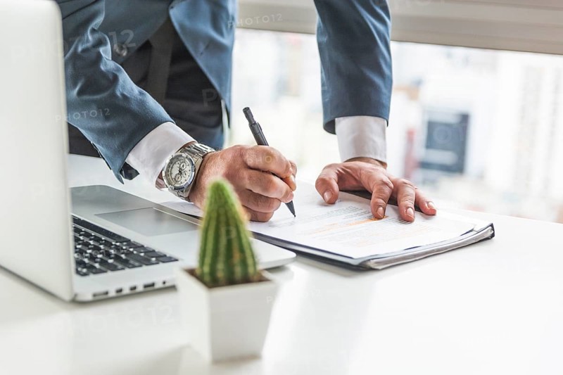 Businessman writing document with pen desk with laptop