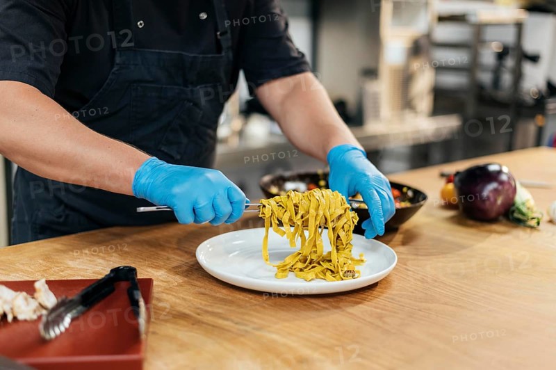 Male chef with gloves putting pasta plate
