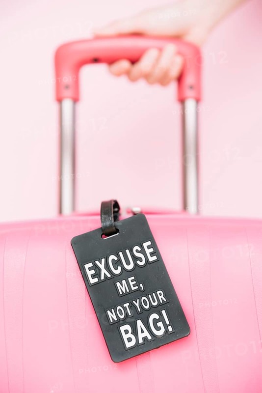 Person s hand holding handle travel suitcase with your bag tag against pink background