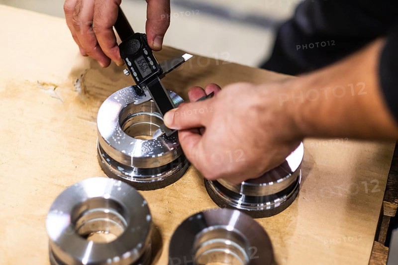 A man uses a digital caliper to measure the size of an opening in a metal part
