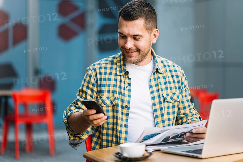 Man with laptop using smartphone cafe