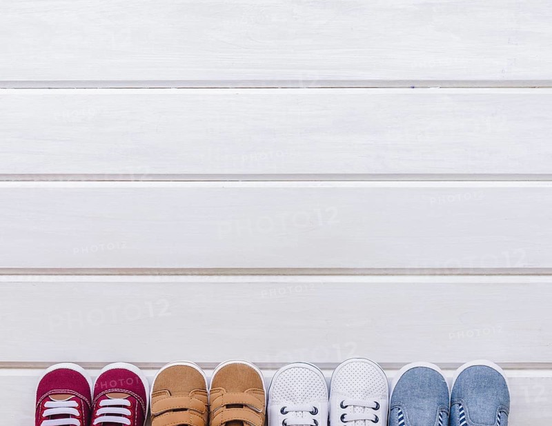 Baby concept with four pairs shoes space wooden surface