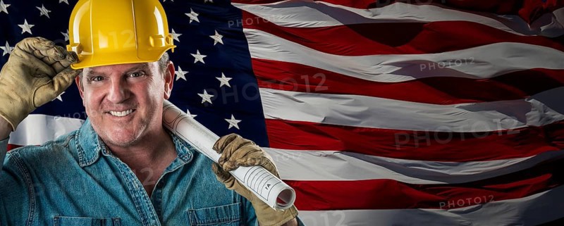 Male contractor wearing blank yellow hardhat over waving american flag background banner