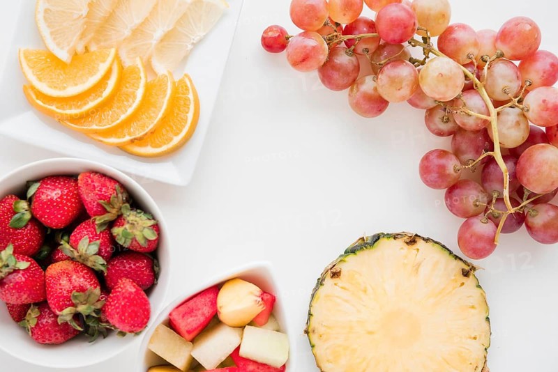 Slices citrus fruit strawberry pineapple watermelon grapes white backdrop