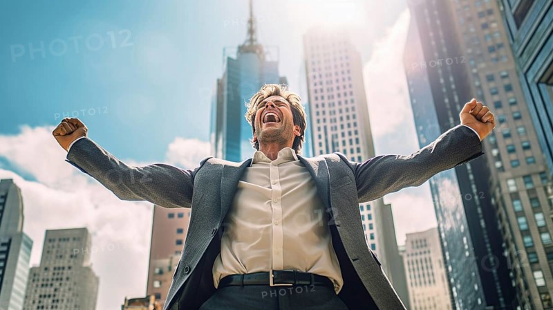 Excited businessman celebrates with his fists in the air with the city in the background