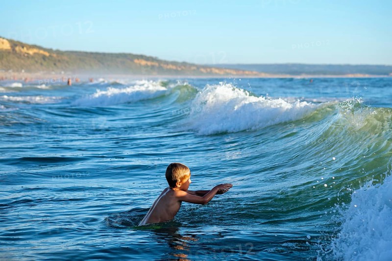 Boy has fun enjoys jumps dives in ocean sea waves of Atlantic Ocean. Fonta da Telha beach