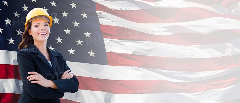 Female contractor wearing blank yellow hardhat and suit over waving american flag background banner