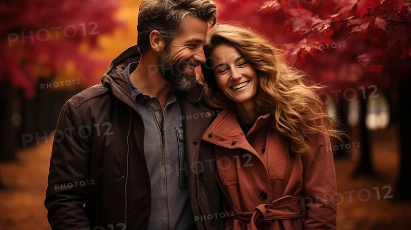 Warmly dressed young loving couple laugh as they enjoy the beautiful fall leaves in the park