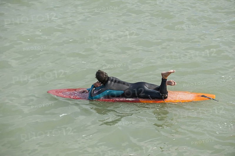 Surfer in wetsuit lying flat on his surfboard in the sea