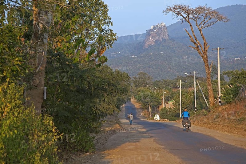 Tourist cycling towards Buddhist monastery on the summit of Taung Kalat near the volcano Mount Popa