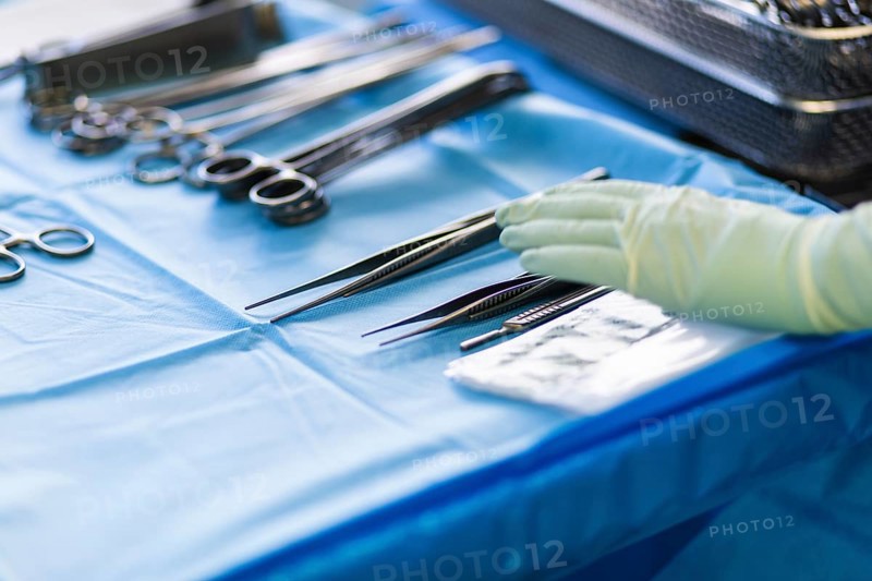 A hand reaches for a pair of tweezers in an operating theatre