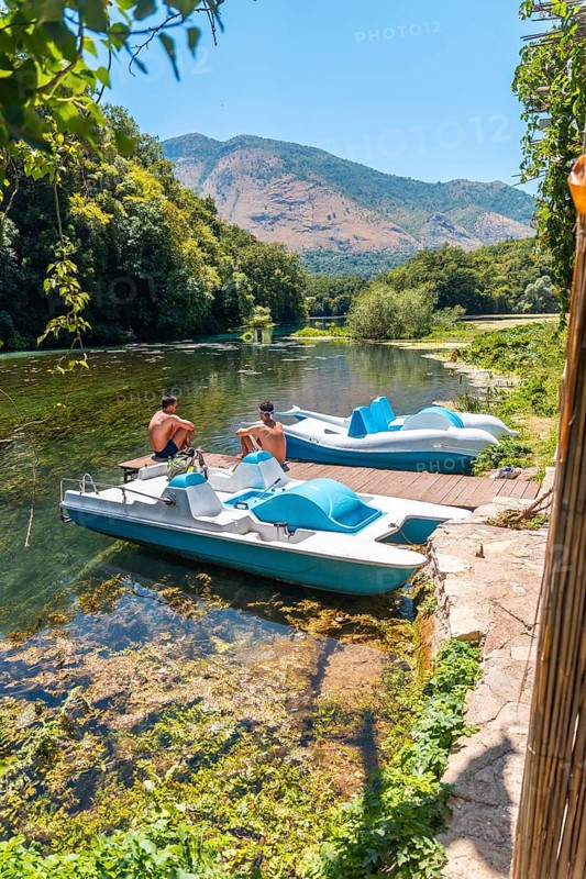 Two men sitting next to some pedalos in the river of The Blue Eye or Syri i kalter