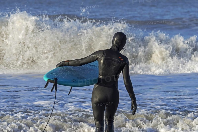Surfer in black wetsuit on the beach entering sea water with surfboard to ride the waves