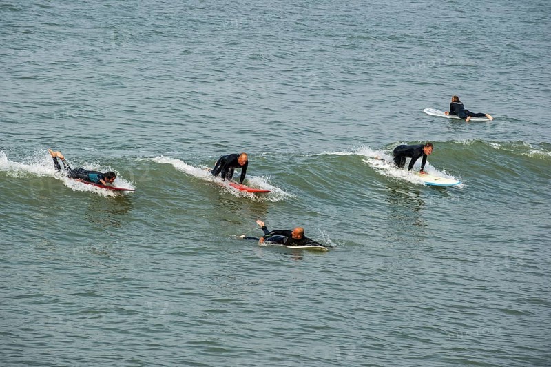 Surfers in wetsuits riding wave on surfboards as it breaks at sea