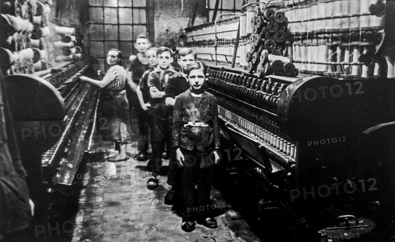 Old black and white archival photograph showing female worker and child labourers posing in spinning mill in the early twentieth century