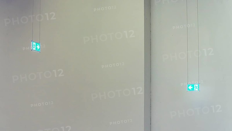Green emergency exit signs in front of white wall
