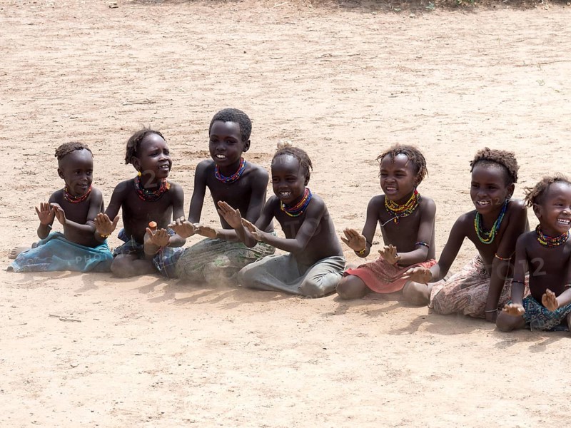 Singing happy children sitting on sandy ground