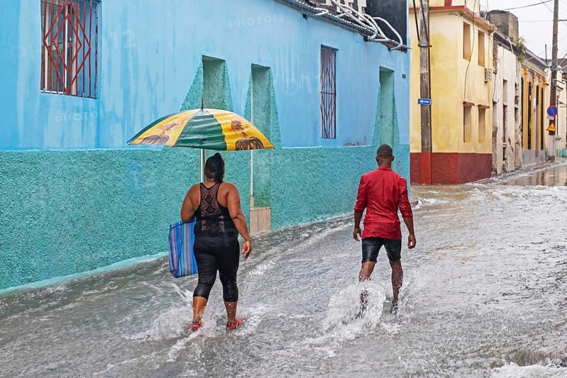 Cubans with umbrellas walking in flooded street during torrential rain in the city Santiago de Cuba on the island Cuba
