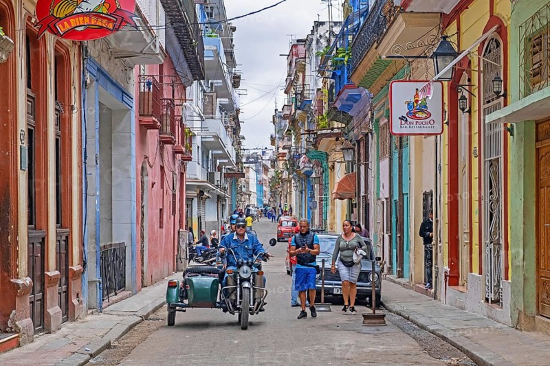 Cubans and motorcycle with sidecar in narrow street with bars and restaurants in the colonial city centre Old Havana