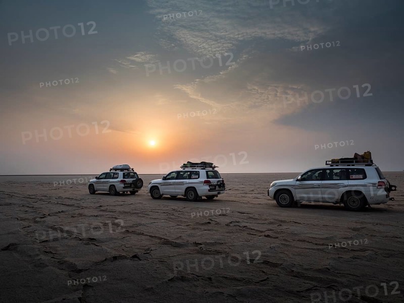 Tourists in off-road vehicles driving on salt desert at sunrise