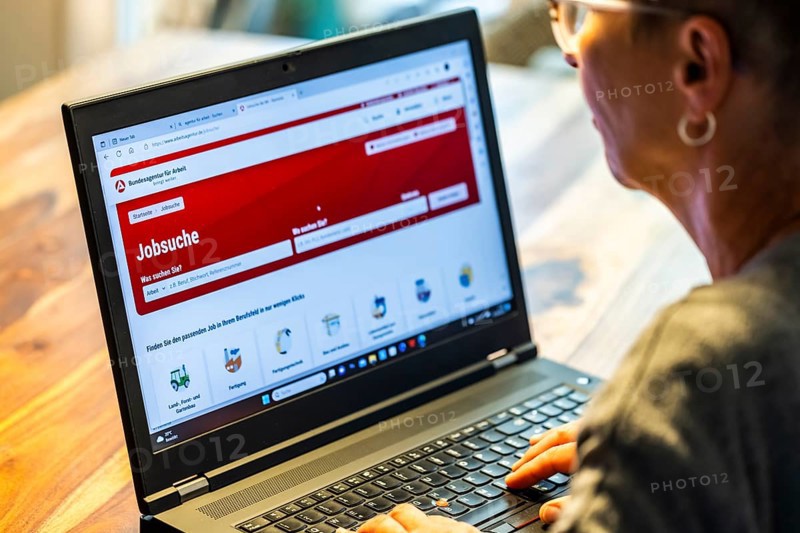 Woman with glasses looking for a job sits at home in front of her notebook and checks the internet site of the Federal Employment Agency for job offers