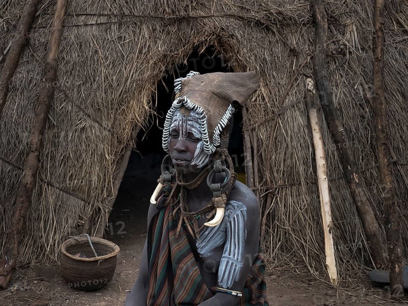 Woman from the Mursi tribe with headdress and face painting in front of her hut
