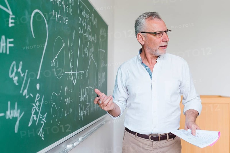 Aged math teacher explaining formula classroom