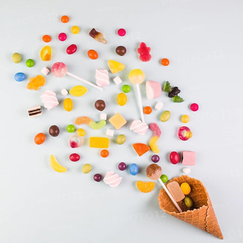 Elevated view various candies with ice cream waffle cone white background