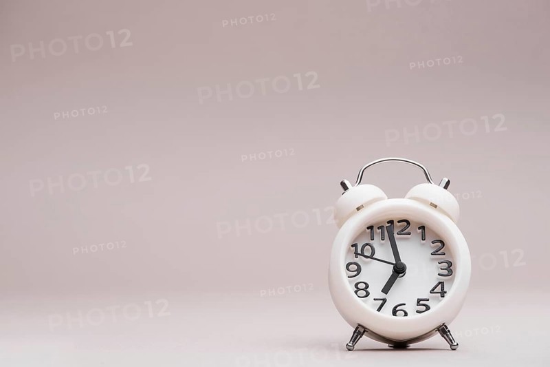 White miniature alarm clock against colored backdrop