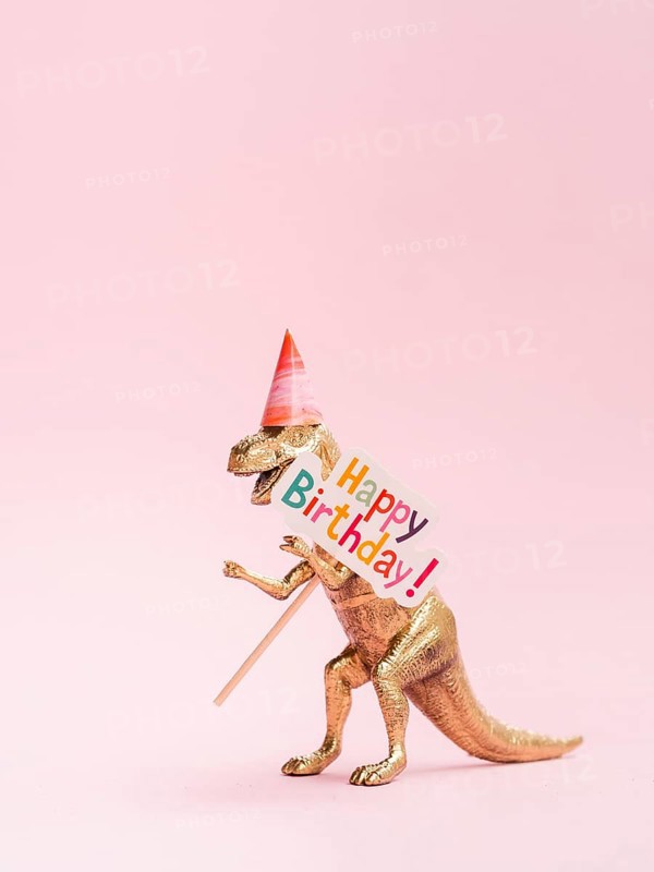 Funny toy dinosaur holding happy birthday sign