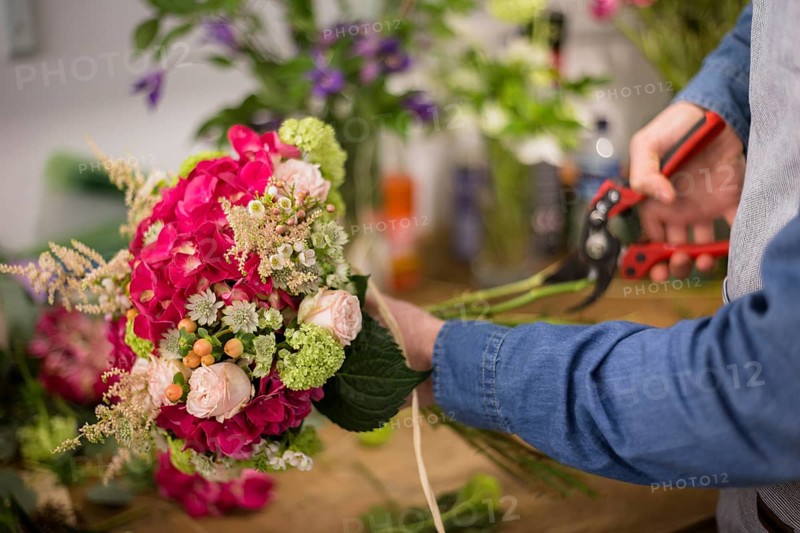 Male florist cutting colorful flower bouquet twigs with pruning shears