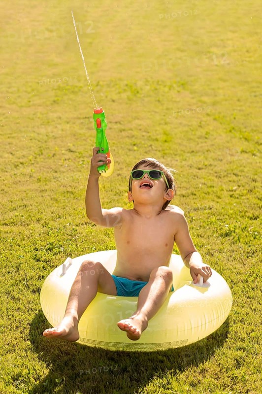 Boy with hat sunglasses playing with water gun