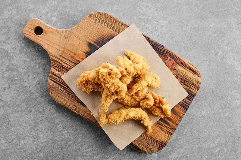 Top view of deep fried chicken nuggets in breading on wooden serving board