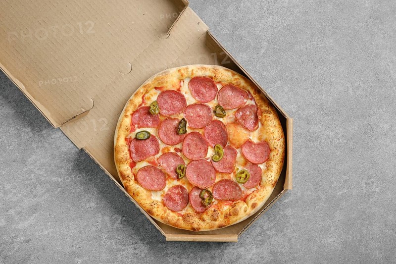 Top view of spicy pizza with sausage and pickled jalapeno pepper in cardboard box