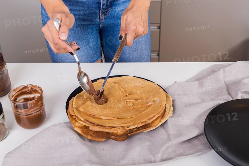 Close up woman spreading peanut butter pancake with spoon knife