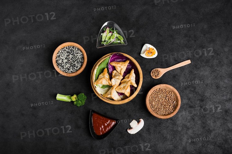 Top view dumplings steamers surrounded with sesame sauce coriander seeds broccoli mushroom black background