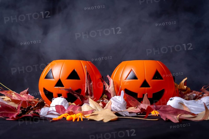 Halloween pumpkins over red autumn leaves and ghosts with smoke on a black background